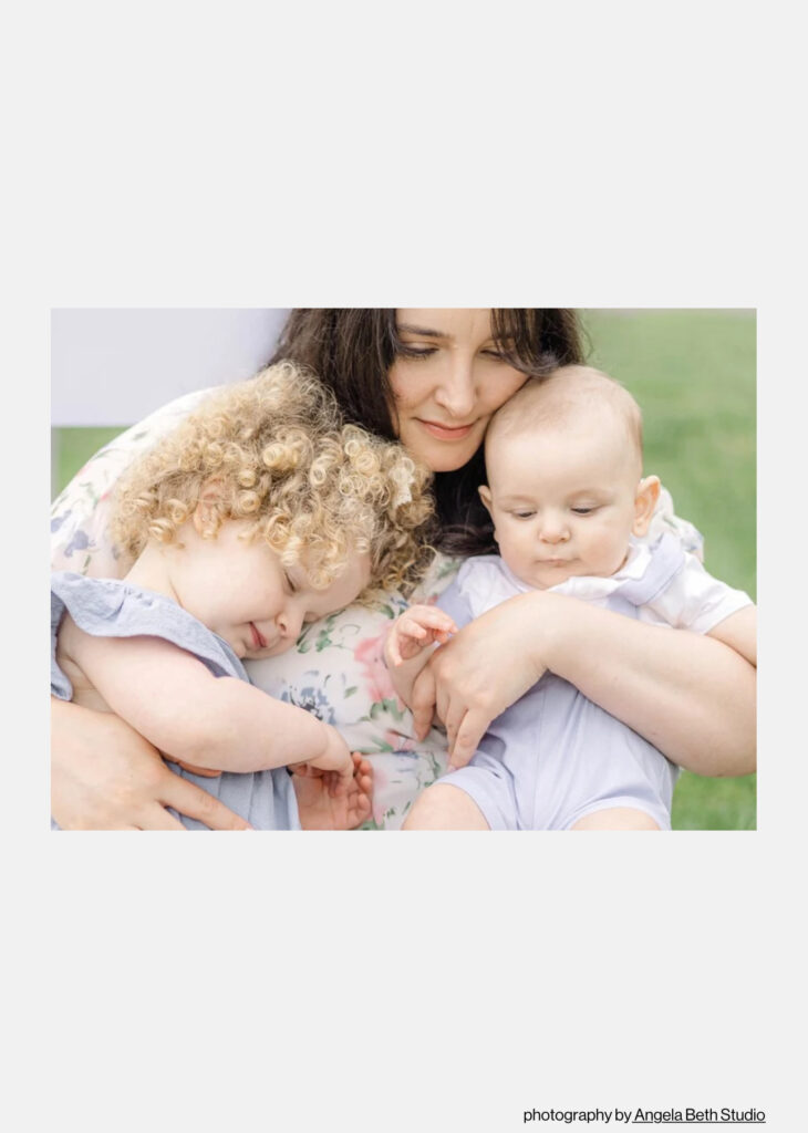 Mother sitting on the grass holding two young children during a peaceful outdoor family session in Bergen County, NJ. Captured by Angela Beth Studio and included in her Petals & Portraits feature in Feels Like Family Magazine.