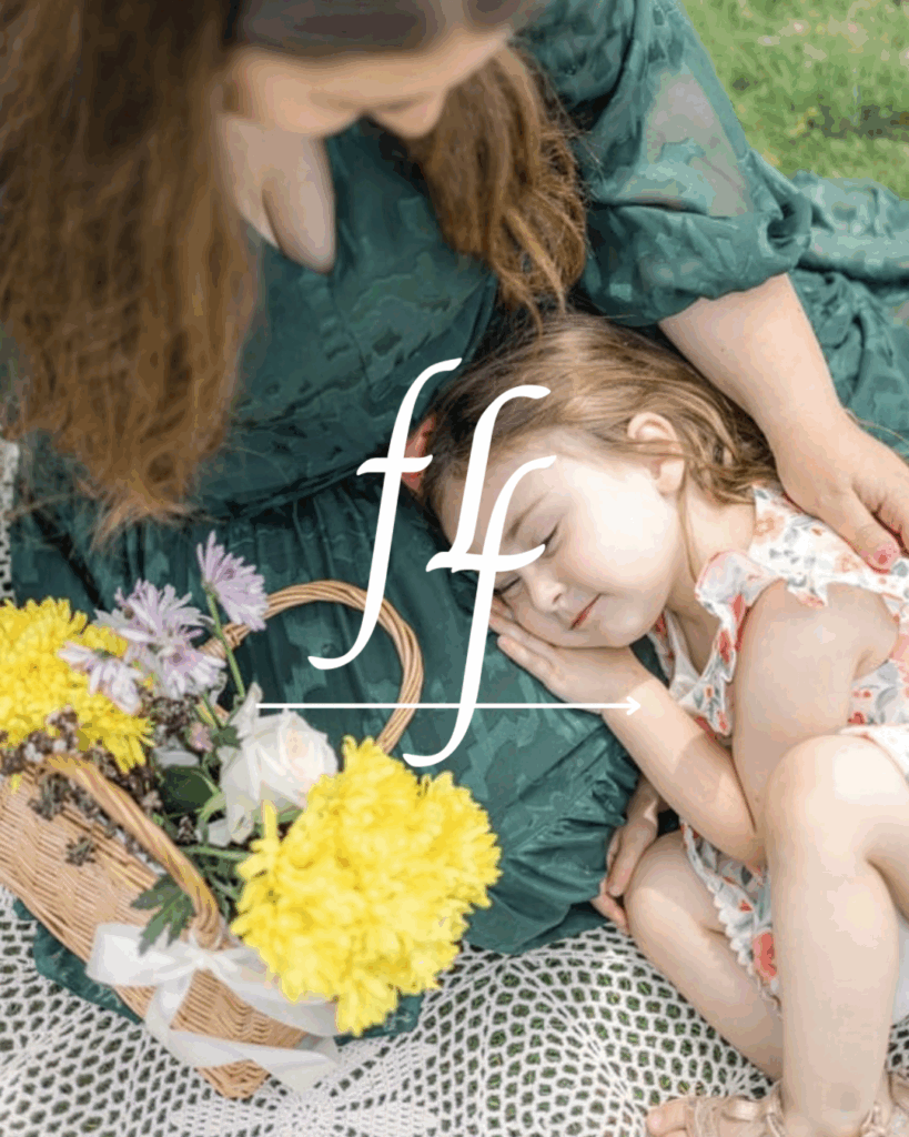 Close-up of a little girl resting on her mother’s lap beside a woven basket filled with yellow and purple flowers. Taken during a Petals & Portraits charity session by Angela Beth Studio in Northern New Jersey.